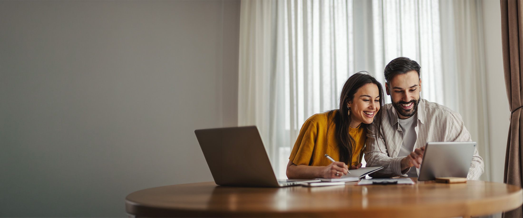 A couple reviewing paperwork together on a laptop and tablet