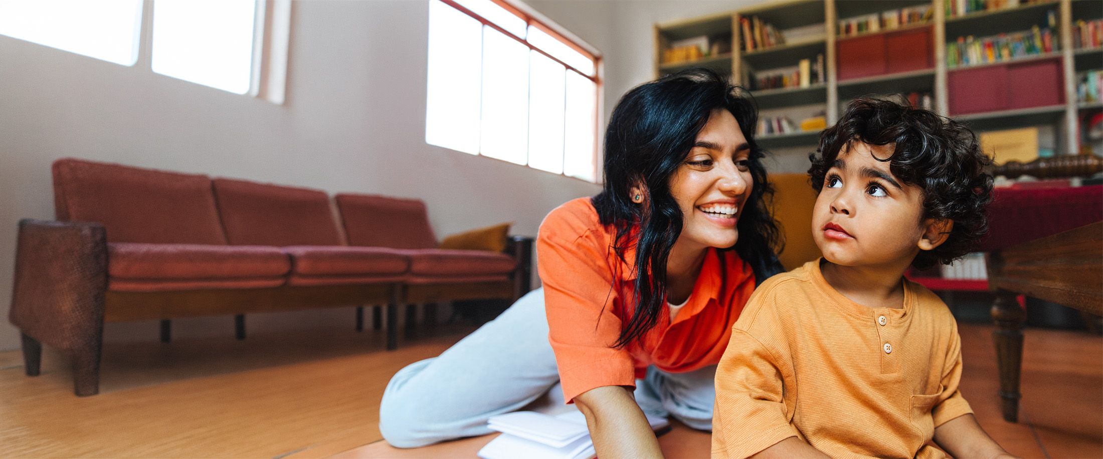 A mother smiling at her young son while they play on the living room floor