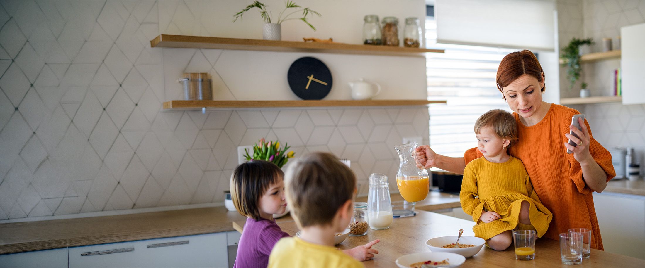 A mother serving breakfast to her three young children in the kitchen
