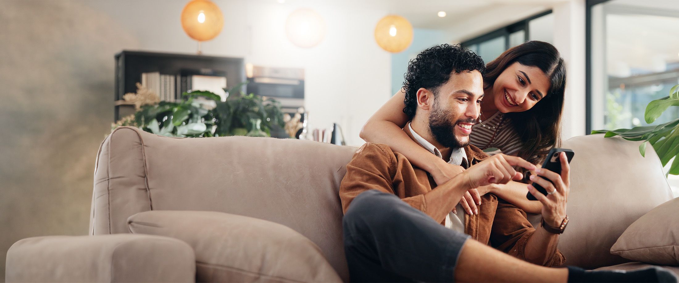 A couple smiling at a phone together on their couch