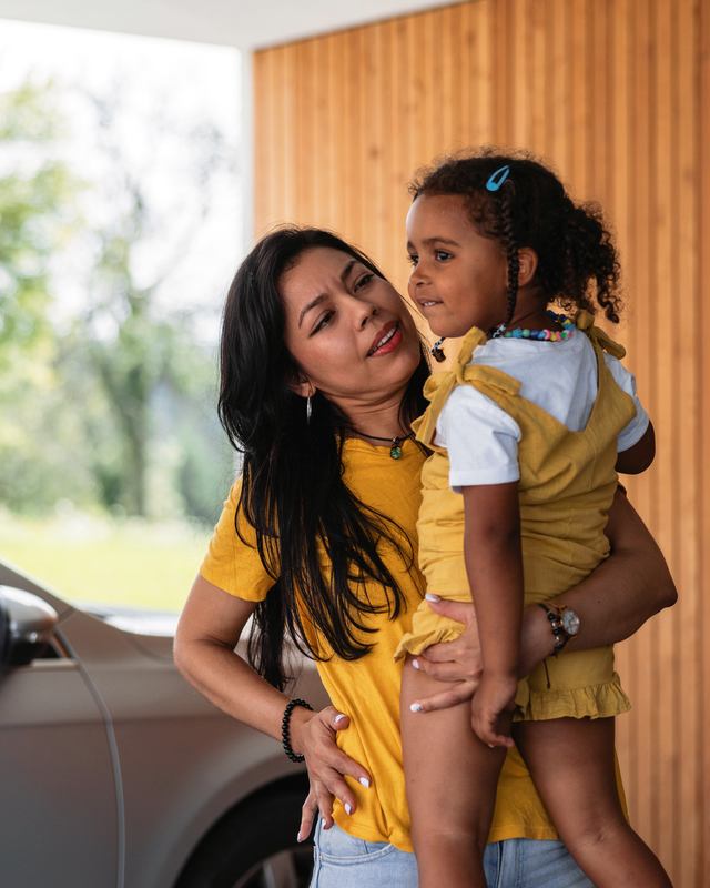 A mother holding her young daughter outside their home